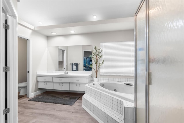 bathroom featuring vanity, hardwood / wood-style floors, a relaxing tiled tub, and toilet