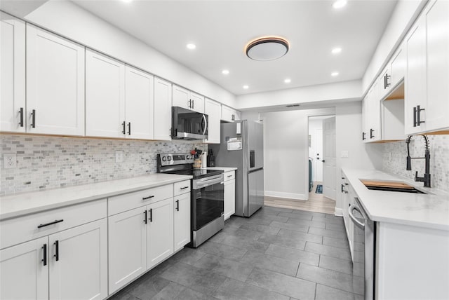 kitchen featuring decorative backsplash, light stone counters, white cabinets, stainless steel appliances, and sink