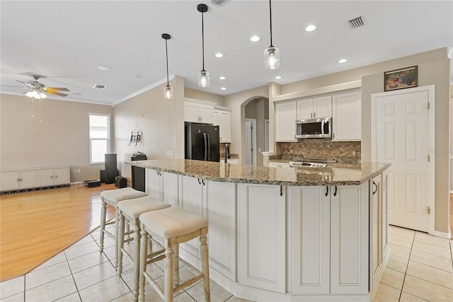 kitchen featuring arched walkways, stainless steel microwave, freestanding refrigerator, a ceiling fan, and light tile patterned floors