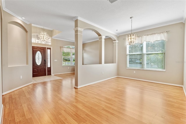 foyer with an inviting chandelier, crown molding, baseboards, decorative columns, and light wood-style flooring