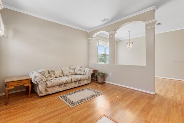 living room featuring an inviting chandelier, ornamental molding, ornate columns, and light hardwood / wood-style floors