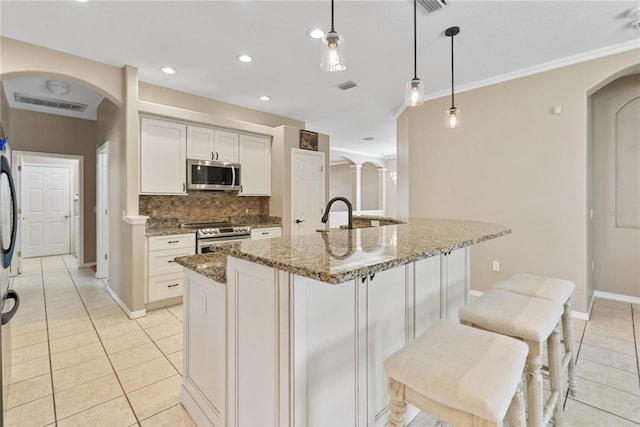 kitchen with stainless steel appliances, hanging light fixtures, light stone counters, and an island with sink