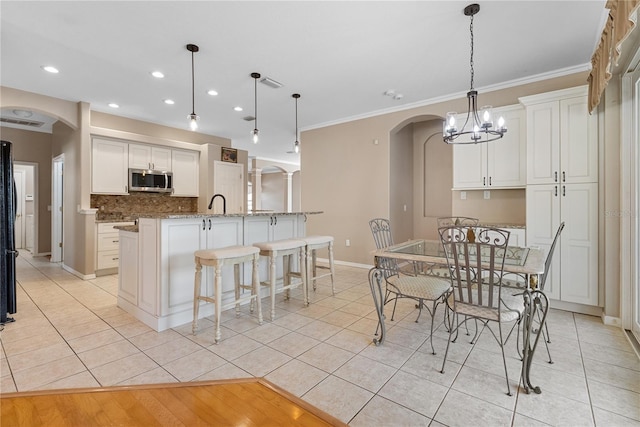 kitchen featuring an island with sink, hanging light fixtures, ornamental molding, white cabinets, and light stone counters