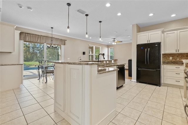 kitchen featuring decorative light fixtures, a center island with sink, plenty of natural light, and black fridge