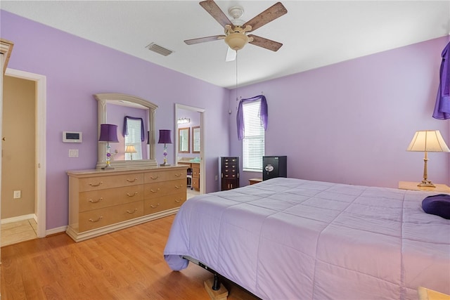 bedroom with a ceiling fan, ensuite bathroom, light wood finished floors, baseboards, and visible vents