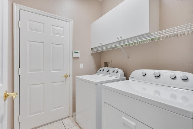 clothes washing area featuring cabinet space, light tile patterned floors, and washer and clothes dryer