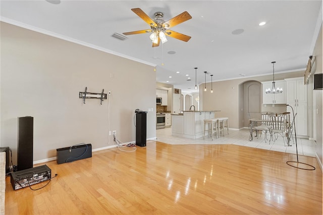 unfurnished living room featuring crown molding, ceiling fan with notable chandelier, and light wood-type flooring