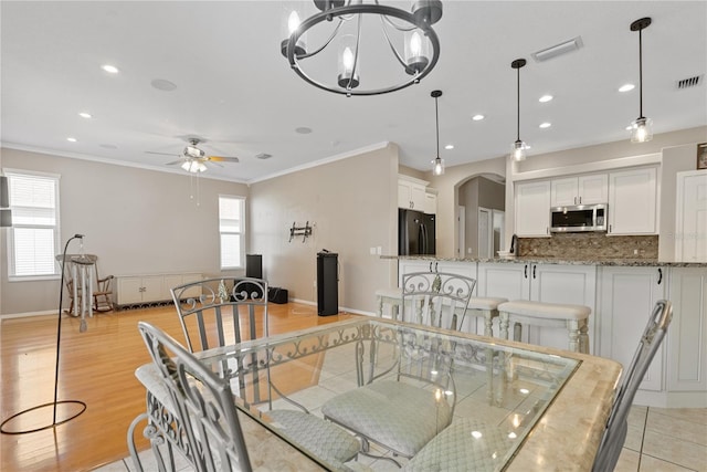 dining room with arched walkways, baseboards, visible vents, ceiling fan with notable chandelier, and crown molding
