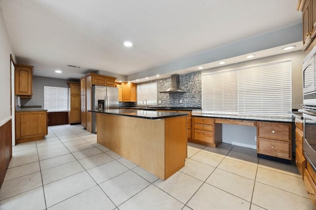 kitchen featuring built in desk, sink, stainless steel refrigerator with ice dispenser, wall chimney exhaust hood, and a center island