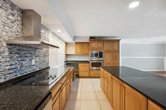 kitchen featuring appliances with stainless steel finishes, dark stone counters, light tile patterned floors, backsplash, and wall chimney range hood