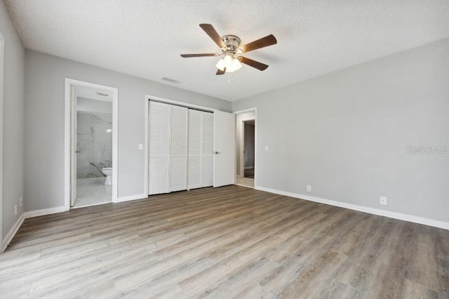 unfurnished bedroom with a textured ceiling, ensuite bathroom, ceiling fan, a closet, and light wood-type flooring