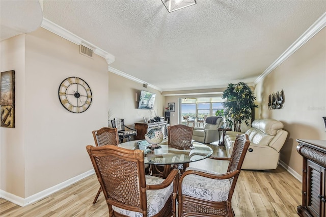 dining room with a textured ceiling, light wood-type flooring, and crown molding