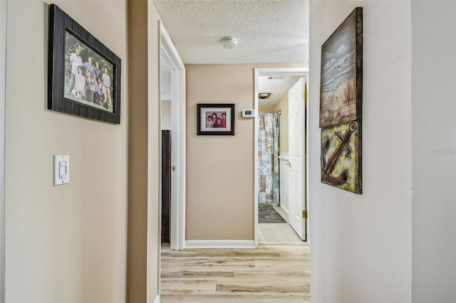 corridor with a textured ceiling and light hardwood / wood-style floors