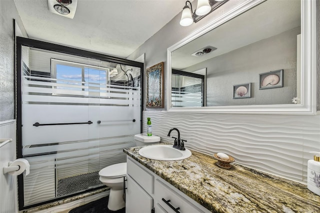 bathroom featuring a textured ceiling, a shower with shower door, vanity, and toilet