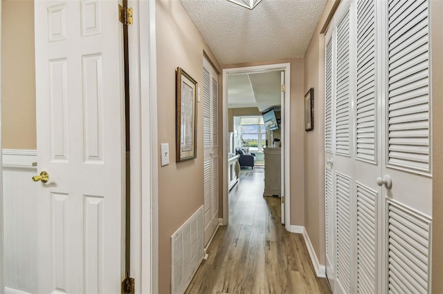 hallway with light wood-type flooring and a textured ceiling