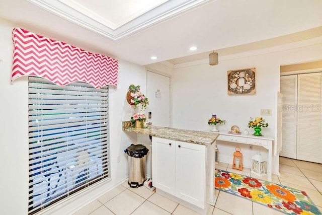 kitchen featuring white cabinets, light tile patterned floors, light stone countertops, and crown molding