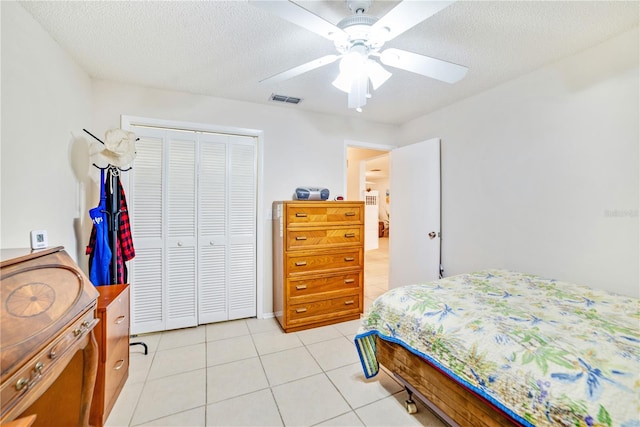 bedroom featuring ceiling fan, light tile patterned floors, a textured ceiling, and a closet