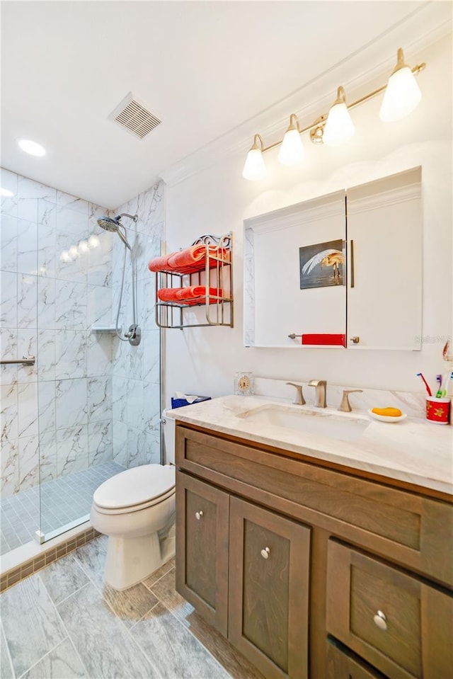 bathroom with a tile shower, crown molding, vanity, and toilet