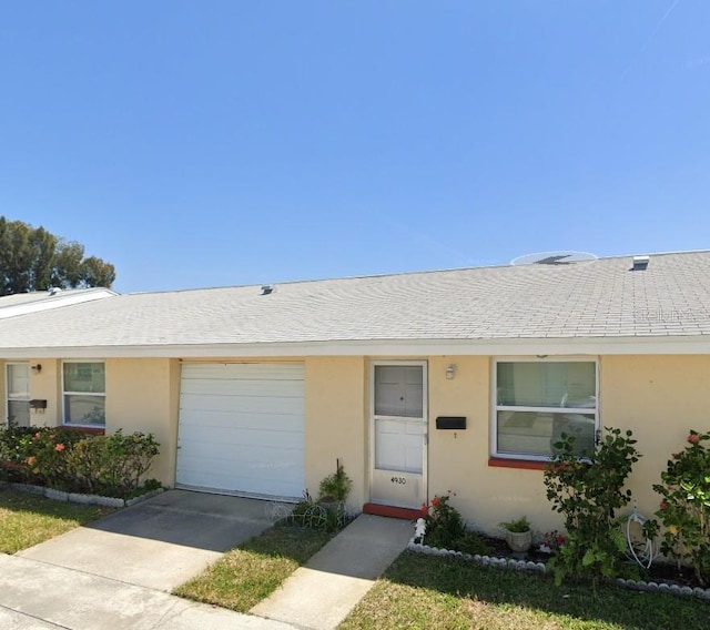 ranch-style house with a shingled roof, concrete driveway, an attached garage, and stucco siding