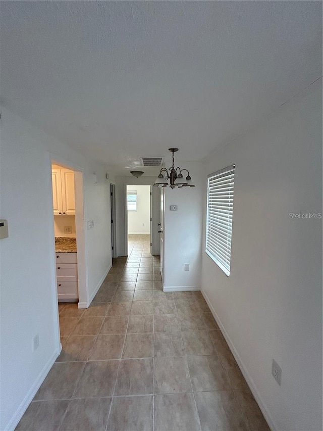 empty room with light tile patterned floors, visible vents, an inviting chandelier, a textured ceiling, and baseboards