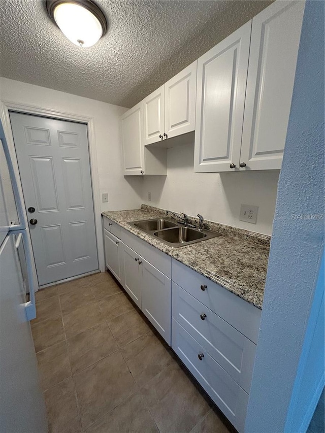 kitchen featuring freestanding refrigerator, white cabinetry, a sink, and a textured ceiling