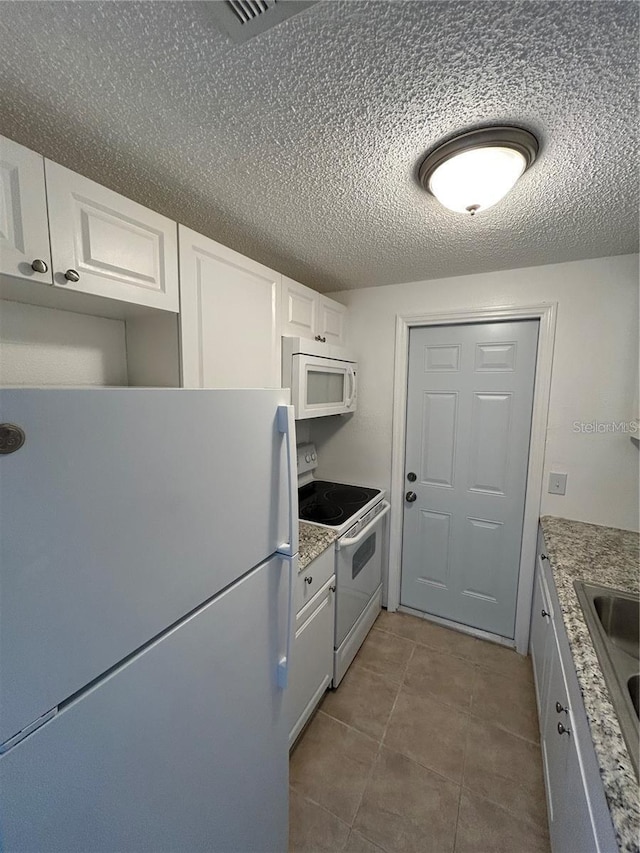 kitchen featuring white appliances, tile patterned flooring, white cabinetry, and a textured ceiling