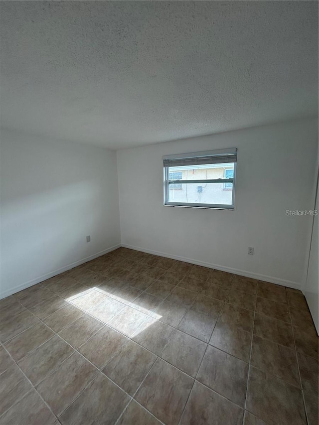 unfurnished room with a textured ceiling, baseboards, and tile patterned floors