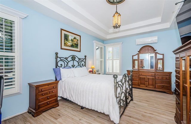 bedroom with a wall mounted air conditioner, multiple windows, and light wood-type flooring