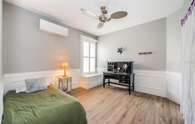 bedroom featuring ceiling fan, light hardwood / wood-style floors, and a wall unit AC