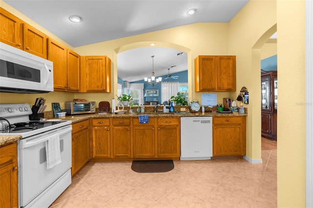 kitchen with pendant lighting, lofted ceiling, white appliances, stone countertops, and a chandelier