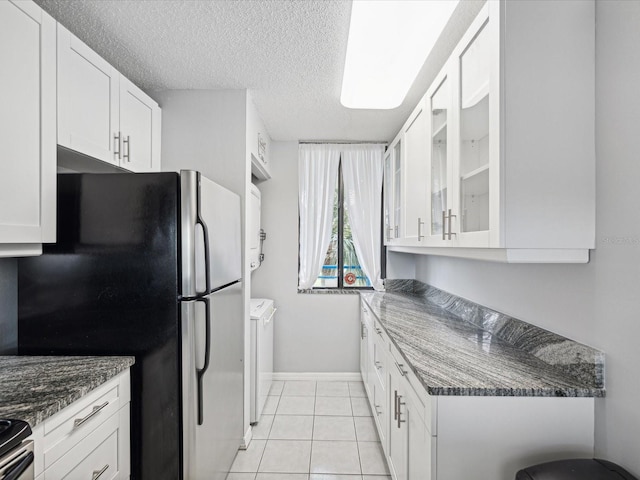 kitchen featuring dark stone counters, white cabinets, light tile patterned floors, and washer and clothes dryer