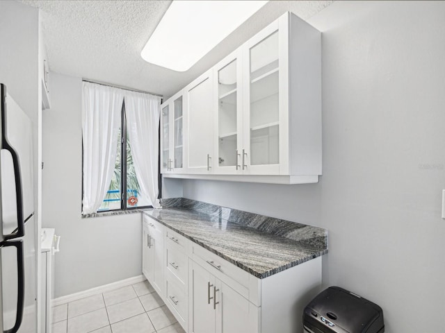 kitchen with dark stone countertops, white cabinets, white fridge, light tile patterned floors, and a textured ceiling