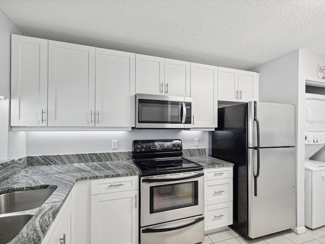 kitchen featuring stacked washer / dryer, appliances with stainless steel finishes, a textured ceiling, and white cabinetry