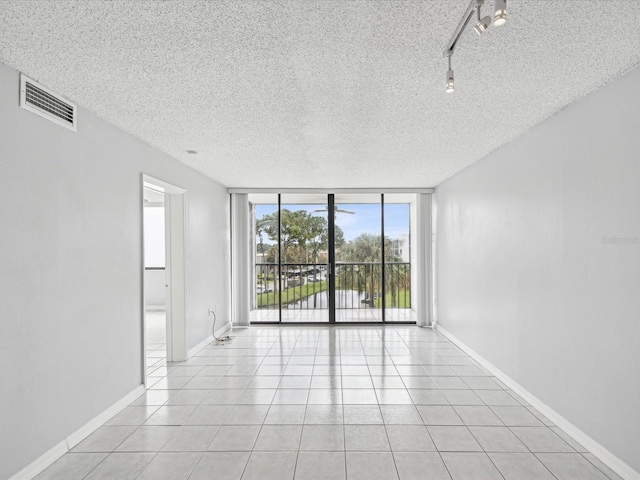 empty room featuring expansive windows, a textured ceiling, light tile patterned floors, and rail lighting