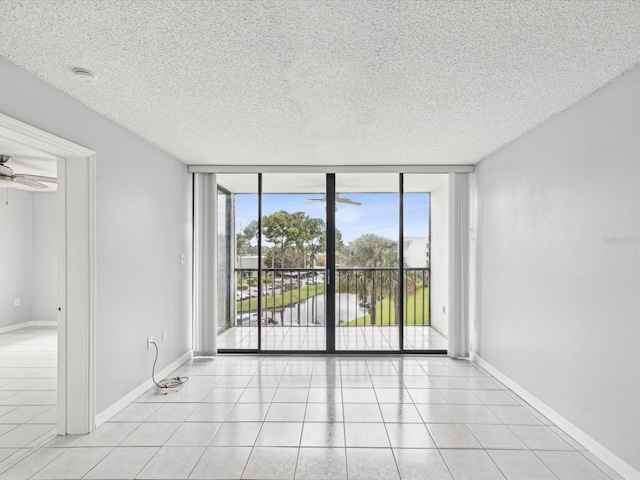 tiled empty room featuring a wall of windows, a textured ceiling, and ceiling fan