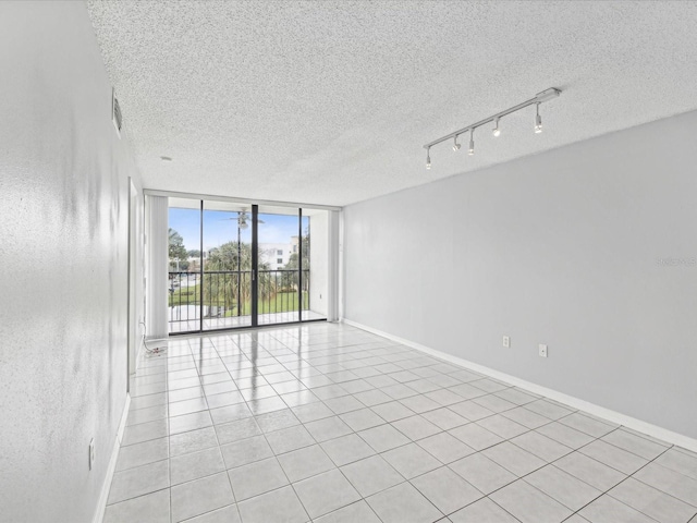 unfurnished room with track lighting, floor to ceiling windows, light tile patterned floors, and a textured ceiling