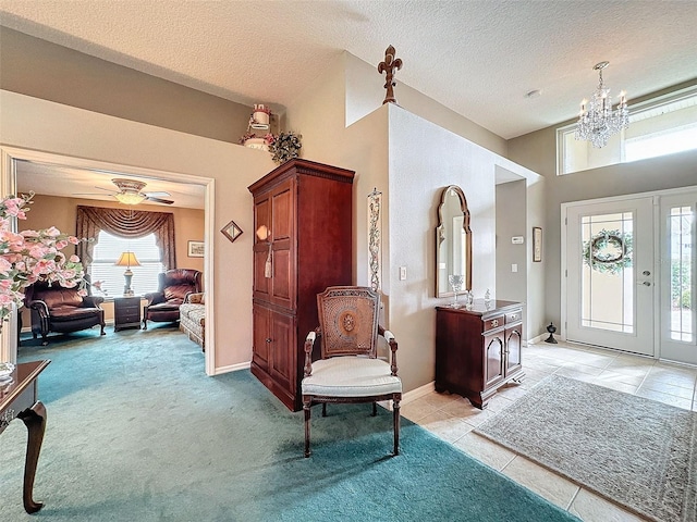 foyer with ceiling fan with notable chandelier, a textured ceiling, and light colored carpet