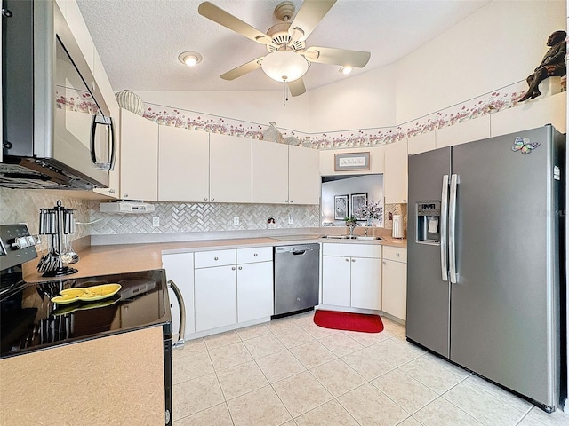 kitchen featuring stainless steel appliances, sink, vaulted ceiling, light tile patterned floors, and white cabinetry