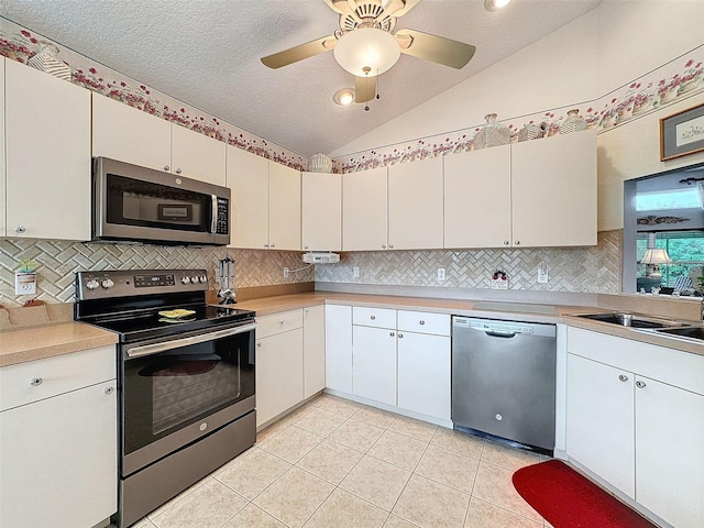 kitchen with lofted ceiling, white cabinets, light tile patterned floors, a textured ceiling, and stainless steel appliances