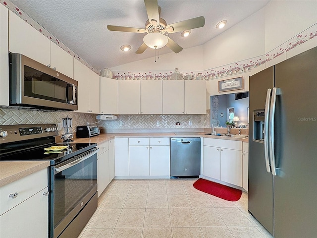 kitchen featuring lofted ceiling, stainless steel appliances, light tile patterned floors, white cabinets, and a textured ceiling