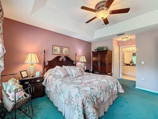 carpeted bedroom with a textured ceiling, ensuite bathroom, a raised ceiling, and ceiling fan