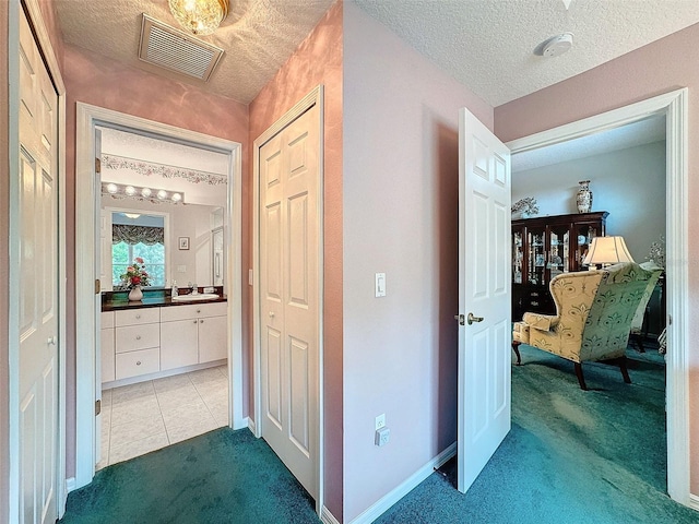 hall featuring a textured ceiling, sink, and dark carpet