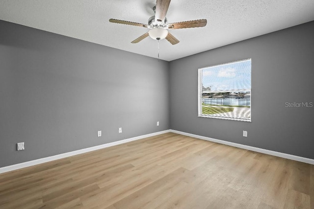 empty room with ceiling fan, light wood-type flooring, and a textured ceiling