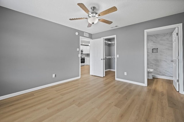 unfurnished bedroom with light wood-type flooring, ensuite bathroom, ceiling fan, a spacious closet, and a closet