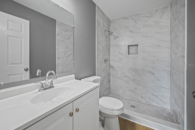 bathroom featuring vanity, toilet, wood-type flooring, and a tile shower