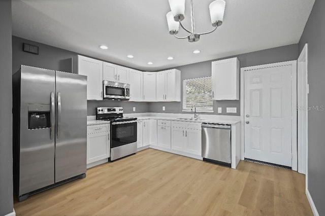 kitchen featuring appliances with stainless steel finishes, sink, decorative light fixtures, light hardwood / wood-style flooring, and white cabinetry