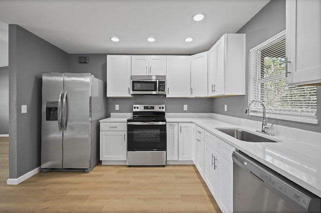 kitchen with stainless steel appliances, white cabinetry, light hardwood / wood-style floors, and sink