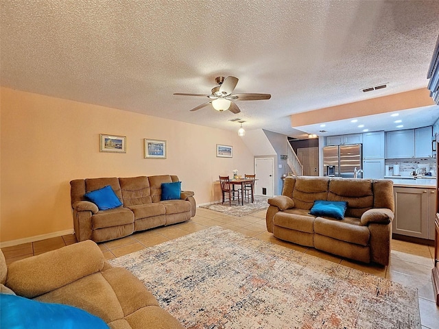 living room with light tile patterned flooring, visible vents, a textured ceiling, and ceiling fan