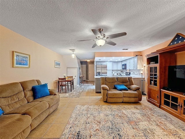 living room with ceiling fan, a textured ceiling, and light tile patterned flooring