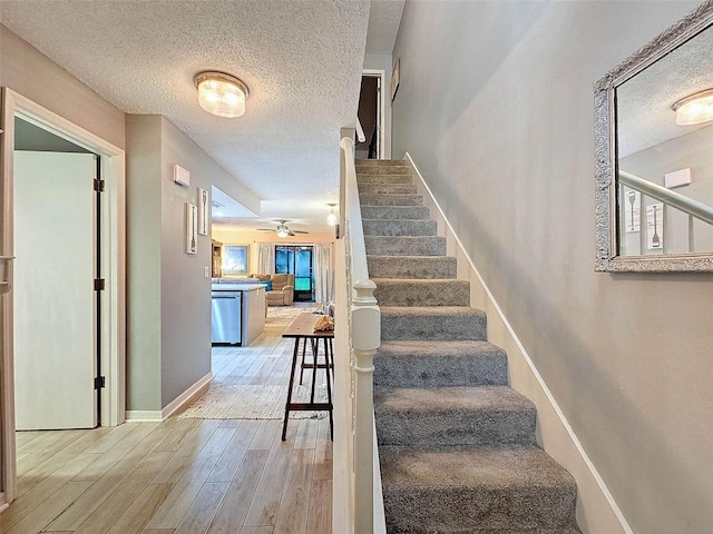 stairs featuring a textured ceiling, a ceiling fan, baseboards, and wood finished floors